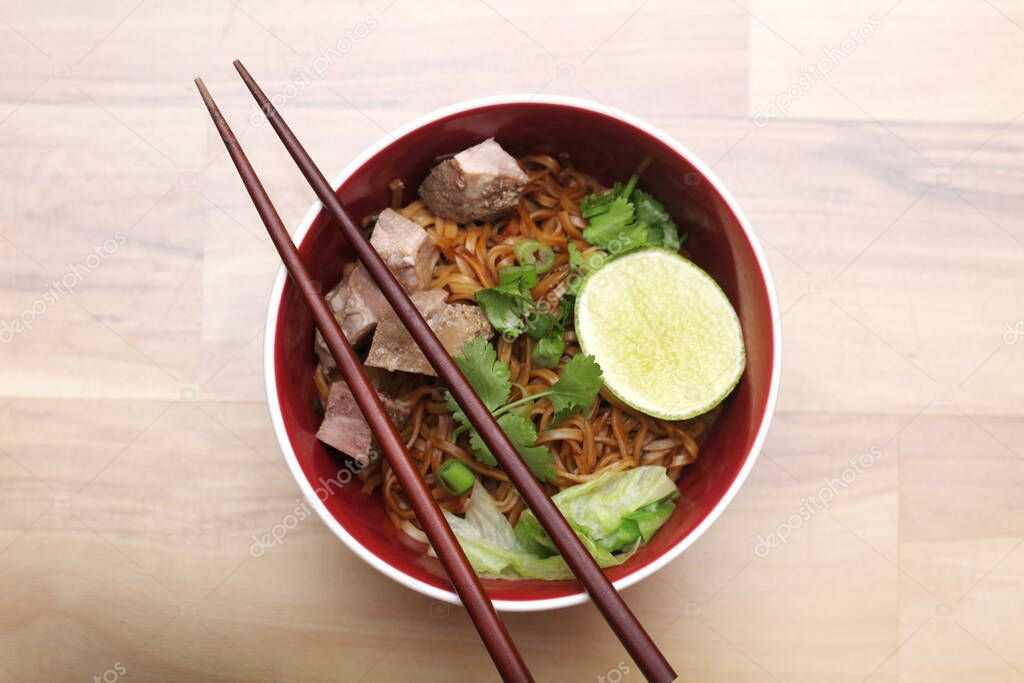 Stewed pork Noodle garnished with coriander, sliced spring onions and lemon wedges. Served on an ash wood table