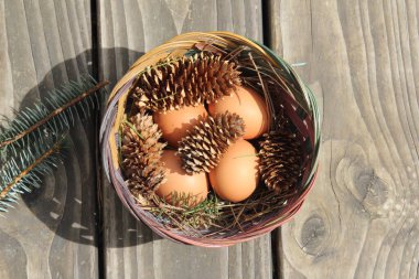 Dört kişilik bir sepetin içinde paskalya yumurtaları ve arka planda çam kozalakları..