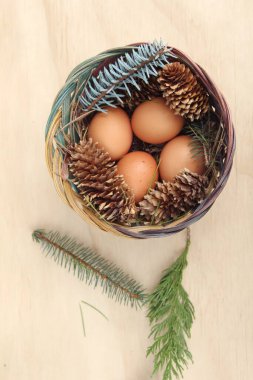 Dört kişilik bir sepetin içinde paskalya yumurtaları ve arka planda çam kozalakları..