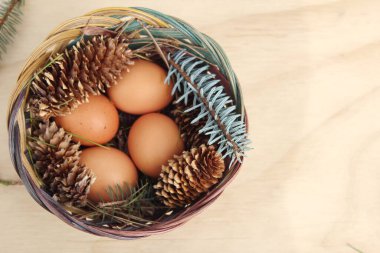 Dört kişilik bir sepetin içinde paskalya yumurtaları ve arka planda çam kozalakları..