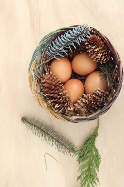 Dört kişilik bir sepetin içinde paskalya yumurtaları ve arka planda çam kozalakları..