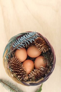 Dört kişilik bir sepetin içinde paskalya yumurtaları ve arka planda çam kozalakları..