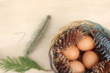 Dört kişilik bir sepetin içinde paskalya yumurtaları ve arka planda çam kozalakları..