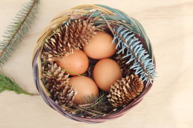 Dört kişilik bir sepetin içinde paskalya yumurtaları ve arka planda çam kozalakları..