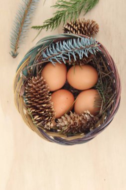 Dört kişilik bir sepetin içinde paskalya yumurtaları ve arka planda çam kozalakları..