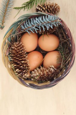 Dört kişilik bir sepetin içinde paskalya yumurtaları ve arka planda çam kozalakları..