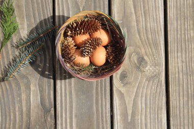 Dört kişilik bir sepetin içinde paskalya yumurtaları ve arka planda çam kozalakları..