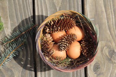 Dört kişilik bir sepetin içinde paskalya yumurtaları ve arka planda çam kozalakları..