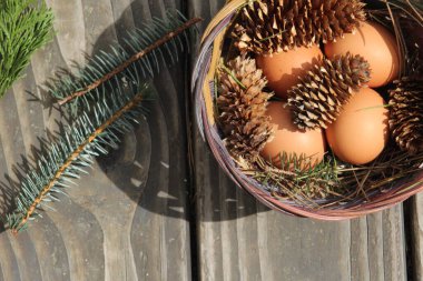 Dört kişilik bir sepetin içinde paskalya yumurtaları ve arka planda çam kozalakları..