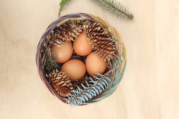 Dört kişilik bir sepetin içinde paskalya yumurtaları ve arka planda çam kozalakları..