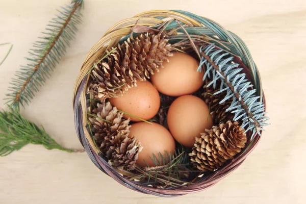 Dört kişilik bir sepetin içinde paskalya yumurtaları ve arka planda çam kozalakları..