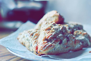 beyaz bir tabakta servis edilen yaban mersinli çörekler ahşap bir masada, modern tonlarda resmedilmiş..