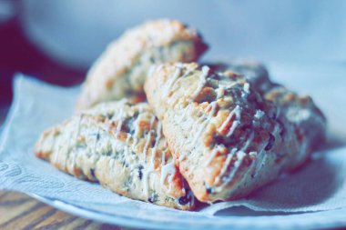 beyaz bir tabakta servis edilen yaban mersinli çörekler ahşap bir masada, modern tonlarda resmedilmiş..