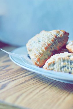 beyaz bir tabakta servis edilen yaban mersinli çörekler ahşap bir masada, modern tonlarda resmedilmiş..