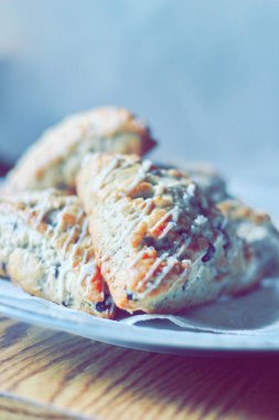 beyaz bir tabakta servis edilen yaban mersinli çörekler ahşap bir masada, modern tonlarda resmedilmiş..
