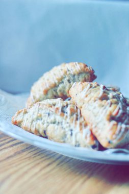 beyaz bir tabakta servis edilen yaban mersinli çörekler ahşap bir masada, modern tonlarda resmedilmiş..