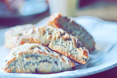 beyaz bir tabakta servis edilen yaban mersinli çörekler ahşap bir masada, modern tonlarda resmedilmiş..