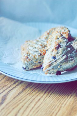 beyaz bir tabakta servis edilen yaban mersinli çörekler ahşap bir masada, modern tonlarda resmedilmiş..