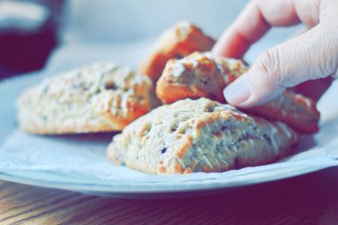 beyaz bir tabakta servis edilen yaban mersinli çörekler ahşap bir masada, modern tonlarda resmedilmiş..