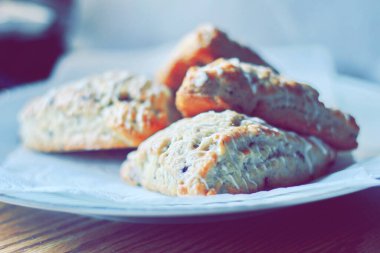 beyaz bir tabakta servis edilen yaban mersinli çörekler ahşap bir masada, modern tonlarda resmedilmiş..