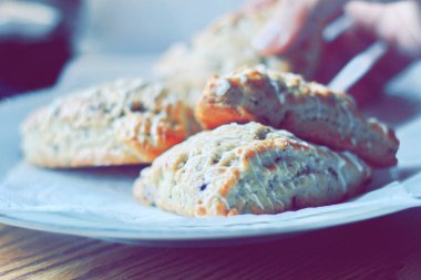 beyaz bir tabakta servis edilen yaban mersinli çörekler ahşap bir masada, modern tonlarda resmedilmiş..