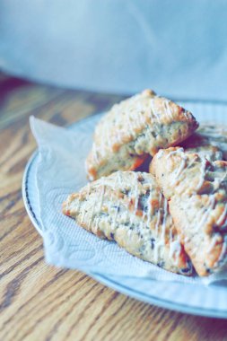 beyaz bir tabakta servis edilen yaban mersinli çörekler ahşap bir masada, modern tonlarda resmedilmiş..