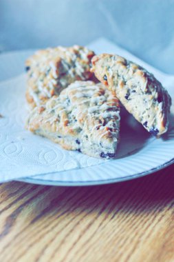 beyaz bir tabakta servis edilen yaban mersinli çörekler ahşap bir masada, modern tonlarda resmedilmiş..