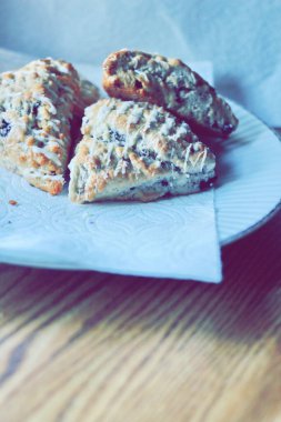 beyaz bir tabakta servis edilen yaban mersinli çörekler ahşap bir masada, modern tonlarda resmedilmiş..