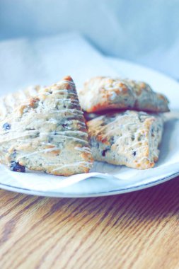 beyaz bir tabakta servis edilen yaban mersinli çörekler ahşap bir masada, modern tonlarda resmedilmiş..