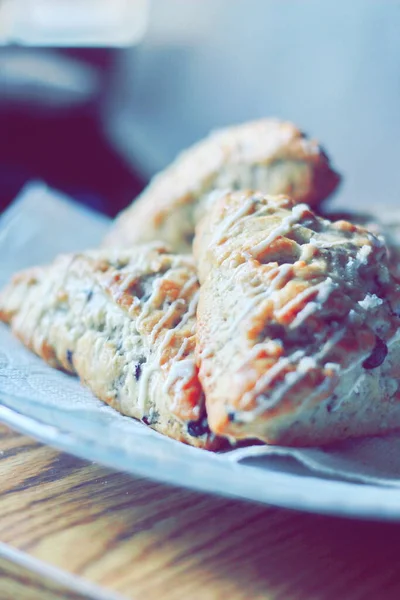 beyaz bir tabakta servis edilen yaban mersinli çörekler ahşap bir masada, modern tonlarda resmedilmiş..