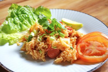 Domuz eti ve kızarmış pilav hafif ahşap bir masada beyaz bir tabakta servis edilir. Limonlu, sebzeli ve domatesli açık ahşap bir masa..