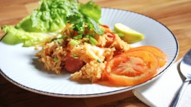 Domuz eti ve kızarmış pilav hafif ahşap bir masada beyaz bir tabakta servis edilir. Limonlu, sebzeli ve domatesli açık ahşap bir masa..