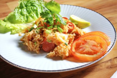 Domuz eti ve kızarmış pilav hafif ahşap bir masada beyaz bir tabakta servis edilir. Limonlu, sebzeli ve domatesli açık ahşap bir masa..