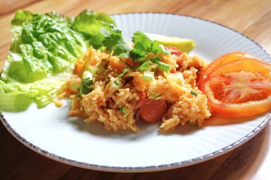 Domuz eti ve kızarmış pilav hafif ahşap bir masada beyaz bir tabakta servis edilir. Limonlu, sebzeli ve domatesli açık ahşap bir masa..