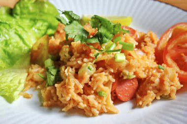 Domuz eti ve kızarmış pilav hafif ahşap bir masada beyaz bir tabakta servis edilir. Limonlu, sebzeli ve domatesli açık ahşap bir masa..