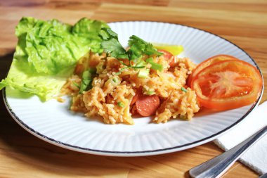 Domuz eti ve kızarmış pilav hafif ahşap bir masada beyaz bir tabakta servis edilir. Limonlu, sebzeli ve domatesli açık ahşap bir masa..