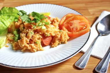 Domuz eti ve kızarmış pilav hafif ahşap bir masada beyaz bir tabakta servis edilir. Limonlu, sebzeli ve domatesli açık ahşap bir masa..