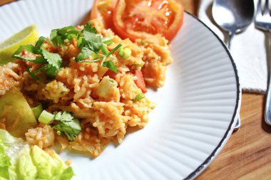 Domuz eti ve kızarmış pilav hafif ahşap bir masada beyaz bir tabakta servis edilir. Limonlu, sebzeli ve domatesli açık ahşap bir masa..