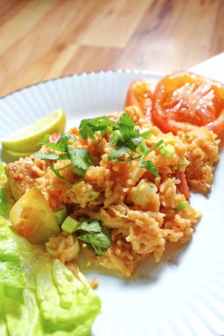 Domuz eti ve kızarmış pilav hafif ahşap bir masada beyaz bir tabakta servis edilir. Limonlu, sebzeli ve domatesli açık ahşap bir masa..