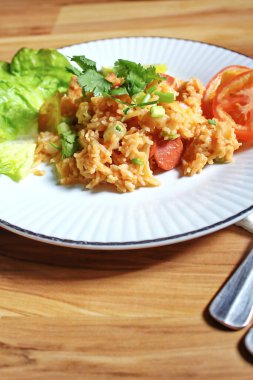 Domuz eti ve kızarmış pilav hafif ahşap bir masada beyaz bir tabakta servis edilir. Limonlu, sebzeli ve domatesli açık ahşap bir masa..