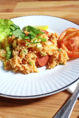 Domuz eti ve kızarmış pilav hafif ahşap bir masada beyaz bir tabakta servis edilir. Limonlu, sebzeli ve domatesli açık ahşap bir masa..