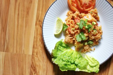 Domuz eti ve kızarmış pilav hafif ahşap bir masada beyaz bir tabakta servis edilir. Limonlu, sebzeli ve domatesli açık ahşap bir masa..