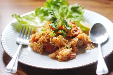 Domuz eti ve kızarmış pilav hafif ahşap bir masada beyaz bir tabakta servis edilir. Limonlu, sebzeli ve domatesli açık ahşap bir masa..