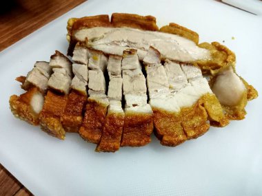 Çıtır domuz dilimlenir ve beyaz bir plastik doğrama tahtasına yerleştirilir..