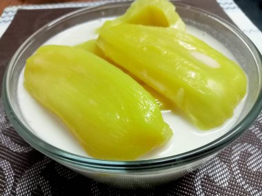 Hindistan cevizi sütlü Jackfruit, sarı iştah açıcı, ahşap bir masaya yerleştirilmiş cam bardakta servis edilir..
