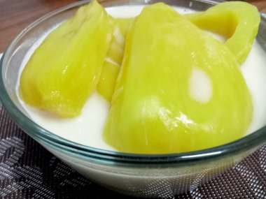 Hindistan cevizi sütlü Jackfruit, sarı iştah açıcı, ahşap bir masaya yerleştirilmiş cam bardakta servis edilir..