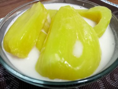 Hindistan cevizi sütlü Jackfruit, sarı iştah açıcı, ahşap bir masaya yerleştirilmiş cam bardakta servis edilir..