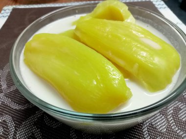 Hindistan cevizi sütlü Jackfruit, sarı iştah açıcı, ahşap bir masaya yerleştirilmiş cam bardakta servis edilir..