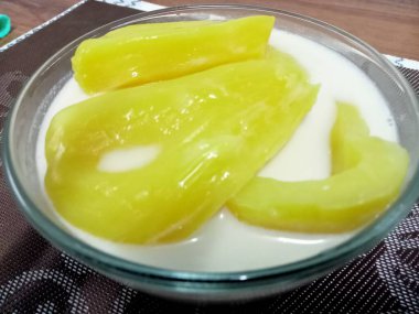 Hindistan cevizi sütlü Jackfruit, sarı iştah açıcı, ahşap bir masaya yerleştirilmiş cam bardakta servis edilir..