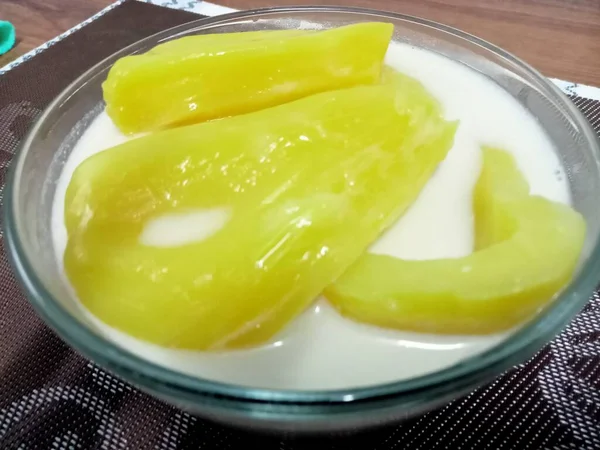 Hindistan cevizi sütlü Jackfruit, sarı iştah açıcı, ahşap bir masaya yerleştirilmiş cam bardakta servis edilir..